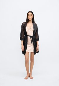 Mustast pitsist kimono heleroosa satiinist slipikleidiga. Slipi kaeluses on pitsdetail. Modell seisab paljajalu.