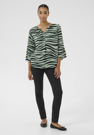 Roheline ja must triibuline pluus kolmeveerandiliste bell-sleeve'idega, mustade slim-fit pükste ja mustade korterite peal. Sile kangastekstuuri.