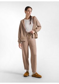 Tvådelat lounge-set i ljusbrun, med en bekväm huoodad jacka och matchande byxor, med dragsko och mjuk textur. Bruna slip-on skor.
