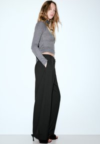 Szary top z długim rękawem w połączeniu z czarnymi, szerokimi spodniami z wysokim stanem. Spodnie mają boczne kieszenie i czystą, uporządkowaną sylwetkę.