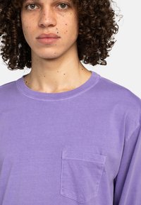 Lavendel Baumwoll-T-Shirt mit kurzen Ärmeln, Rundhalsausschnitt und einer linken Brusttasche. Weiche Textur und minimalistisches Design.
