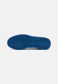 Blue athletic shoe outsole with textured grip patterns, featuring a prominent Reebok logo and a curved design for flexibility.