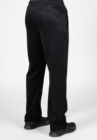 Zwarte sportieve broek van een gladde stof, met een tapered fit, elastische tailleband, zijzakken en een gematteerd paneel aan de zijkant.