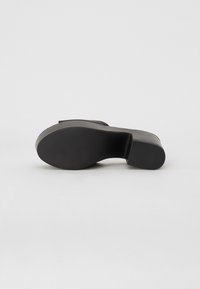 Black high-heeled shoe with a smooth upper, rounded toe, and a textured sole. Features a chunky heel and minimal detailing.