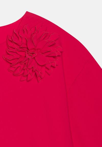 Živý fuchsiový top s viacvrstvovou kvetinovou aplikáciou na ľavom ramene. Vyrobený z hladkej látky s voľným strihom a detailom na bočnom šve.