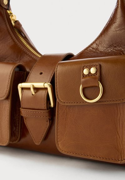 Bolsa de mão de couro castanho com uma textura suave, detalhes em metal dourado, alça ajustável e dois bolsos frontais com fecho de botão.