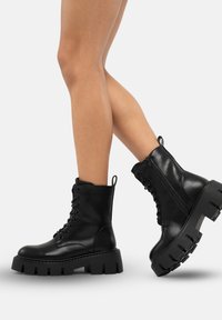 Stivaletti neri in pelle con suola platform chunky, stringati sulla parte anteriore e con una zip laterale. Presentano un anello sul retro per indossarli facilmente.