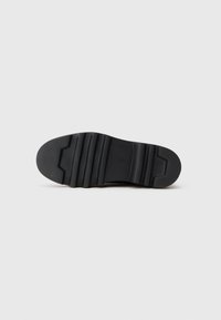 Sole nera di scarpa con una texture rigata e scanalature distintive per la trazione, realizzata in materiale gommoso resistente.