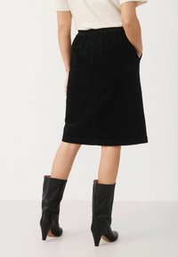 Black corduroy skirt with elastic waistband, knee-length, side pockets, paired with knee-high black leather heeled boots.
