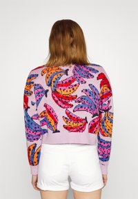 Afskåret sweater i lys lilla strik med multicolorerede bananmønstre i pink, orange og blå. Ribbekanter ved ærmer og søm.