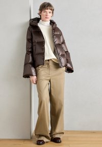 Pehme, tumedat pruunid lukuga jope kapuutsiga, kombineeritud kõrge vöökohaga beežide laia lõikega pükstega ja pruunide jalanõudega. Silmatorkavalt sujuv materjal.