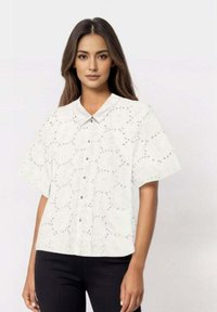 White short-sleeve button-up shirt with a textured fabric featuring eyelet cutouts, rounded collar, and a relaxed fit.