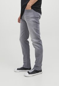 Jeans vaqueros grises de corte slim, con costuras cosidas, bolsillos delanteros y combinados con zapatillas negras. Textura suave y diseño casual.