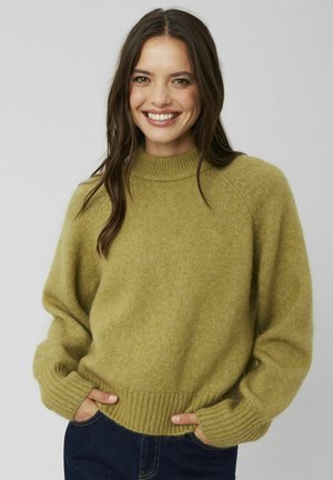 Pull en maille vert olive avec un col montant, des poignets et un ourlet côtelés, et une coupe décontractée. Le tissu est doux et texturé.