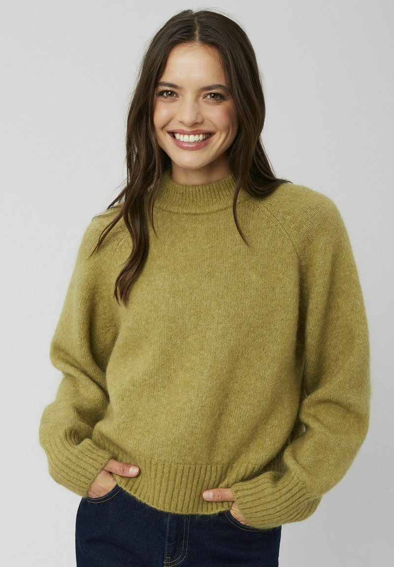Pull en maille vert olive avec un col montant, des poignets et un ourlet côtelés, et une coupe décontractée. Le tissu est doux et texturé.