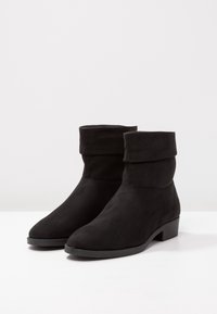 Bottines en daim noir avec un revers, bout rond et petit talon carré. Texture lisse et design minimaliste.