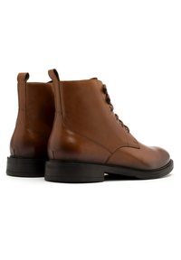 Brązowe skórzane botki sięgające kostki o gładkim wykończeniu, zaokrąglonym nosku, sznurowanym przodzie i niskim czarnym obcasie, z subtelnym detalem szwu.