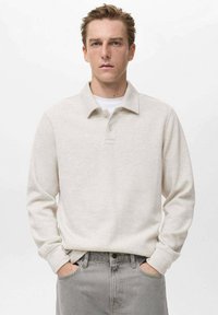Polo a maniche lunghe color beige chiaro, realizzato in tessuto morbido, con colletto tradizionale, patta con due bottoni e polsini a costine.