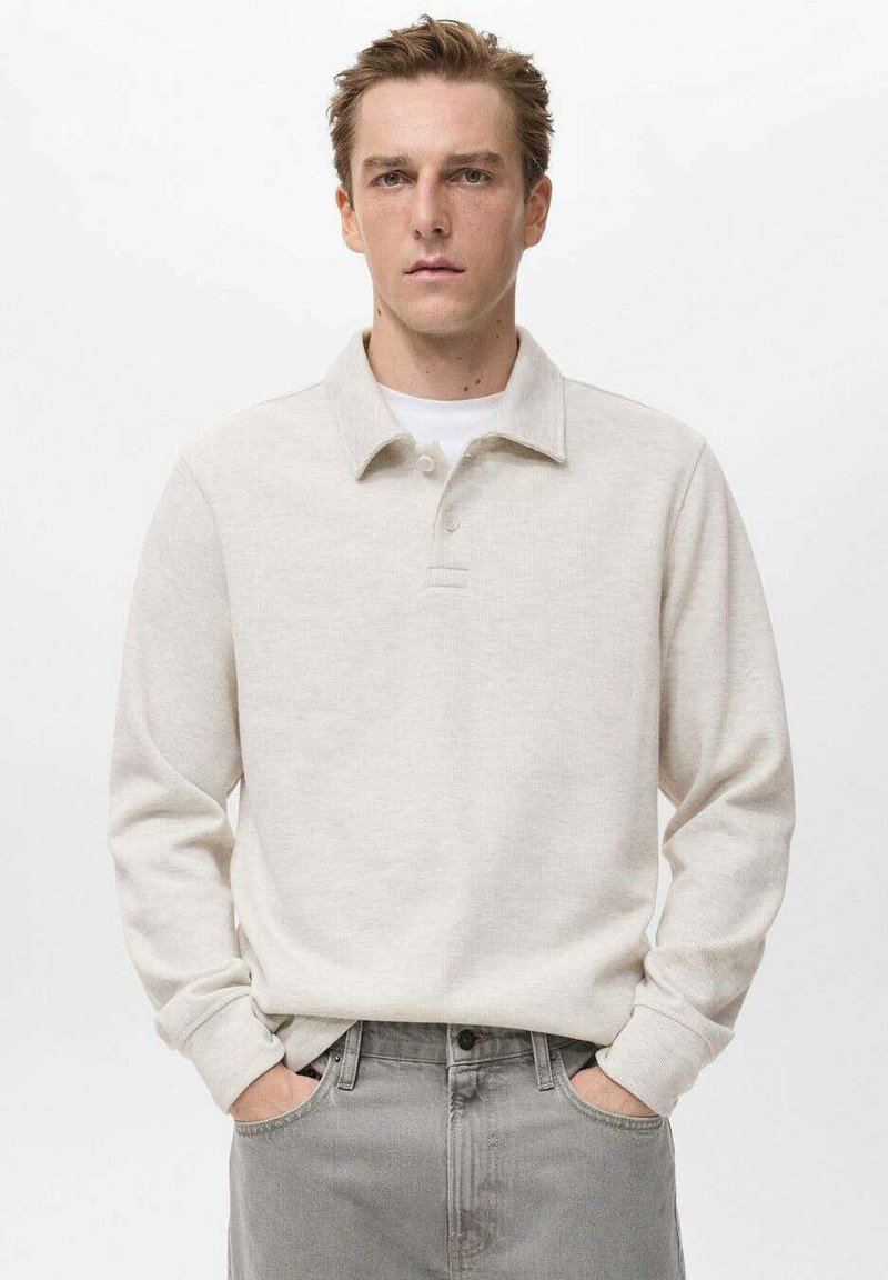 Polo a maniche lunghe color beige chiaro, realizzato in tessuto morbido, con colletto tradizionale, patta con due bottoni e polsini a costine.