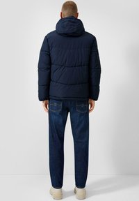 Marineblauwe gewatteerde jas met een capuchon, voorzien van gestikte secties. Draag als bovenkleding op een blauwe jeans en lichtgekleurde sneakers. Eenvoudig ontwerp, matte textuur.