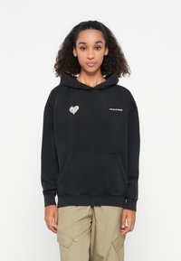Zwarte hoodie van zachte stof, met een buidelzak aan de voorkant, geribbelde manchetten en een klein hartontwerp en logo op de borst.