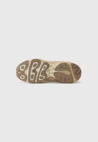 La suola della scarpa presenta un design in gomma testurizzata nei toni beige e marrone, con modelli di scolpitura distintivi e il nome del marchio, "New Balance."