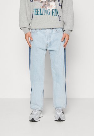 Jasnoniebieskie dżinsy z ciemnoniebieskimi bocznymi panelami noszone z szarą bluzą z nadrukiem orła oraz białoszare sneakersy.