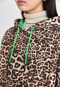 Luipaardprint hoodie met een zachte textuur, voorzien van groene koorden en een contrasterende lichte coltrui eronder.