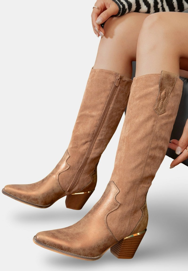 Bottes en suède beige jusqu'au genou avec des bouts pointus, des accents texturés et un talon empilé avec un détail doré. Fermeture éclair sur le côté pour faciliter l'enfilage.