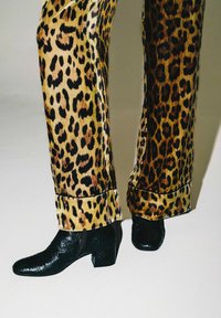 Pantaloni in velluto testurizzato con stampa leopardata, dalla vestibilità dritta, abbinati a stivaletti neri con texture a coccodrillo e tacco largo.
