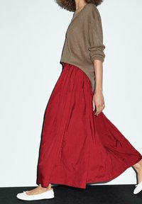 Ruskea, oversize neulepaita, joka on valmistettu neuloksesta, yhdistetty virtaavaan punaiseen maxi-hameeseen, jota täydentävät valkoiset ballerinat. Yksinkertainen ja rento muotoilu.