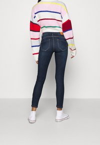Jeans ajustados azules con cintura alta y bolsillos traseros, combinados con un suéter de rayas multicolores que presenta franjas en rosa, rojo y verde.