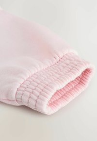 Puño de sudadera de algodón rosa con banda elástica recolectada, que presenta una textura suave y un acabado liso. El interior es de un rosa ligeramente más claro.