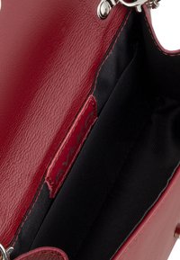 Interno della borsa in pelle rossa caratterizzato da una texture liscia, hardware argentato e una fodera nera con logo.