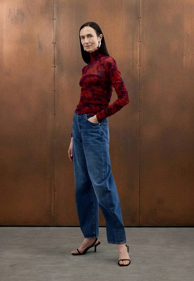 Haut à manches longues à motifs rouges et violets, associé à un jean taille haute à jambes larges bleu clair et à des sandales noires à talons hauts.