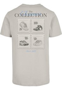 Lys grå T-shirt med et baggrafik af fire frimærkedesign, hvor hver viser forskellige sneakersstyles med tekst og priser.
