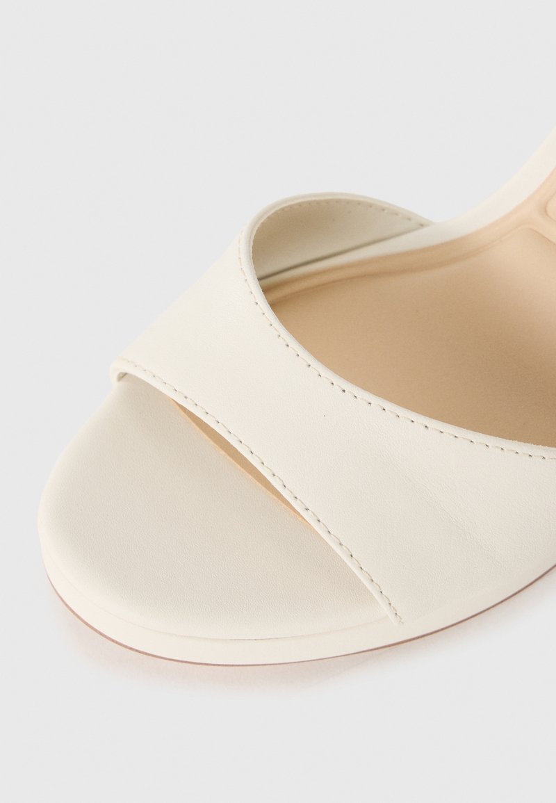 Sandalia abierta color crema con tira de cuero suave y suela acolchada, mostrada en primer plano sobre un fondo blanco.