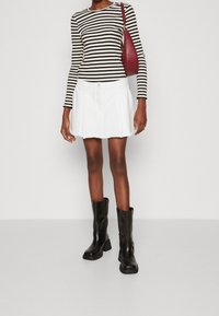 Czarna i biała bluzka w paski z długim rękawem, biała plisowana spódnica oraz czarne kozaki za kolano, przełamane bordową torebką jako kontrastem i dodatkiem.