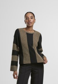 Sweter robiony na drutach z szerokimi pionowymi paskami w czerni i beżu. Projekt ma okrągły dekolt i długie rękawy, z teksturowanym wykończeniem.