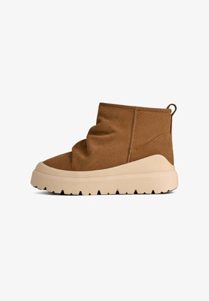 Stivaletto alla caviglia in finta pelle scamosciata marrone con design morbido, suola spessa beige chiaro e linguetta posteriore. Tomaia testurizzata e suola con battistrada spesso.