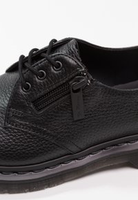 Chaussure en cuir noir présentant une surface texturée, un bout arrondi, un design à lacets, une fermeture éclair latérale et une semelle contrastante avec détail de surpiqûres.