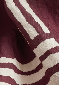 Textiel met een kastanjebruine achtergrond en gedurfde, gestructureerde crèmekleurige strepen. Katoenen weving onthult complexe patronen en een zachte, natuurlijke afwerking.