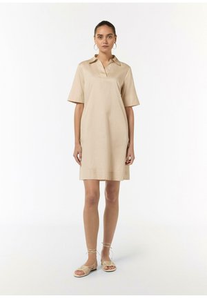 Beige Kurzarmkleid mit Kragen, aus weichem Stoff gefertigt. Das Kleid hat eine lockere Passform und reicht über die Knie, kombiniert mit Sandalen mit Riemchen.