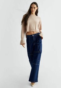 Maglione corto rosa chiaro con maniche lunghe, abbinato a jeans cargo a gamba larga blu scuro con tasche applicate e cuciture a contrasto.