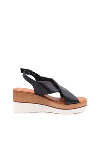 Sandalo in pelle nera con zeppa e cinturini incrociati, sottopiede color cuoio e suola in gomma bianca. Cinturino posteriore regolabile per una vestibilità sicura.
