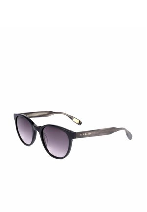 Occhiali da sole rotondi neri con lenti scure sfumate e sottili aste grigie, marchiati Ted Baker sulle aste.