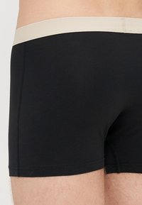 Črne boksarice iz raztegljive tkanine, z belo obrobo. Oblikovanje vključuje ravne šive in prilegajoč obliko.