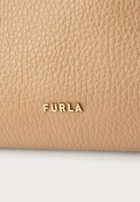 Piele texturată bej cu un model de granulație vizibilă, având un logo aurit "FURLA". Fundalul este alb.