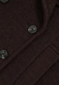 Burgundská vlněná bunda s texturovaným povrchem, vybavená dvěma černými knoflíky s názvem značky. Jednoduchý, přiléhavý design s bočními kapsami.