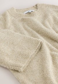 Beiger flauschiger Pullover aus strukturiertem Garn. Verfügt über einen Rundhalsausschnitt und eine lockere Passform, mit sichtbarem Etikett am Kragen.